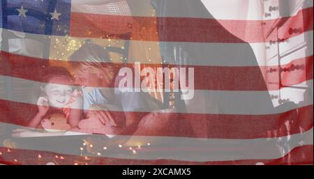 Amerikanische Flagge winkt gegen kaukasische Mutter und Tochter unter einer Decke zu Hause. amerikanisches Unabhängigkeits- und Festkonzept Stockfoto