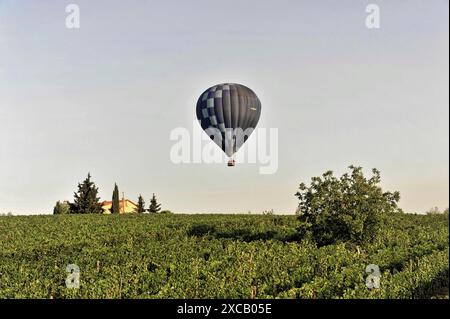 Heißluftballons, Tavarnelle, Toskana, Italien, Europa, ein blauer Heißluftballon schwingt über einem grünen Feld mit einem Landhaus und Bäumen Stockfoto