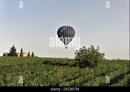 Heißluftballons, Tavarnelle, Toskana, Italien, Europa, ein blauer Heißluftballon schwimmt über einem grünen Feld mit einem Landhaus und Bäumen im Stockfoto