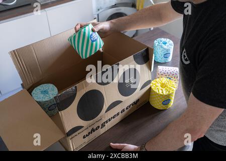 Ein Mann, der eine Papierrolle aus Papier nimmt, die mit dem Firmenlogo aus einem Lieferkarton verpackt ist. Konzept: Nachhaltiges Toilettenpapier Stockfoto