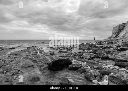 Ein Schwarzweiß-Blick auf den Leuchtturm Beachy Head und die Klippen und den zerklüfteten Strand Stockfoto