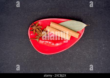 Blick von oben auf Sternanis, auch bekannt als Badian, rote Chili, Abschleppstück von Zimt mit Tejpatta, auch bekannt als Indian Bay Leaf, isoliert auf schwarzem Backgr Stockfoto