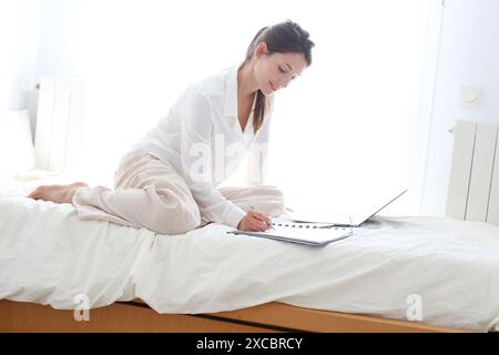 Frau sitzt auf dem Bett und mit laptop Stockfoto