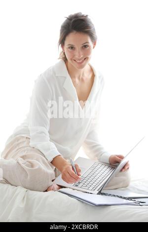 Frau sitzt auf dem Bett und mit laptop Stockfoto