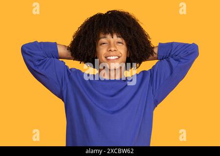 Lächelnder junger Mann mit lockigem Haar, der sich auf Gelb zurücklehnt Stockfoto