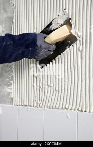 Vorbereitung der Wand mit Klebmörtel vor dem Fliesen mit einer gezackten Putzkelle, Neubauten im Bau, Baustelle Stockfoto