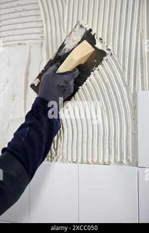 Vorbereitung der Wand mit Klebmörtel vor dem Fliesen mit einer gezackten Putzkelle, Neubauten im Bau, Baustelle Stockfoto