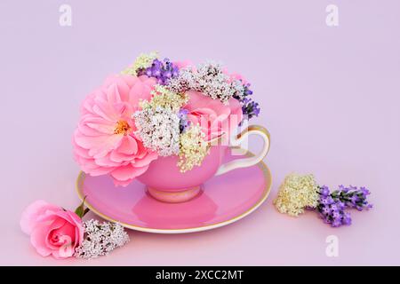 Surreale Rosen-, Holunder-, Baldrian- und Lavendelblüten in Teetasse auf Rosa. Fun Food medizinische Kräutermedizin Design. Flora hat adaptogene Eigenschaften. Stockfoto