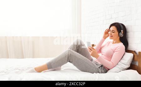 Junge Frau, die sich im Bett entspannt und Musik hört Stockfoto