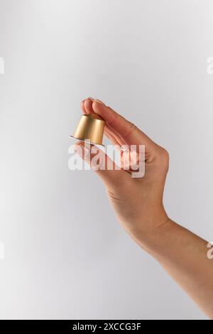 Hand mit einer einzelnen goldenen Kaffeekapsel auf weißem Hintergrund Stockfoto