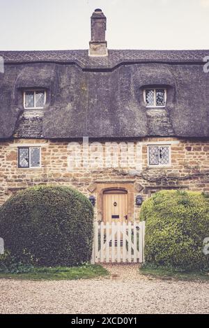 Ein charmantes Steinhaus mit einem Strohdach und einem weißen Pflückzaun in ländlicher Umgebung. Stockfoto
