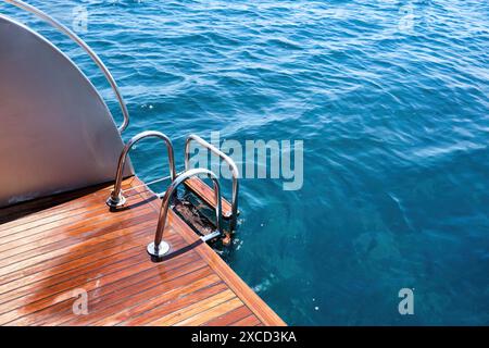 Holzdeck aus Teakholz und Metallleiter einer Motoryacht über dem Meer. Stockfoto