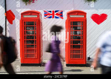 Klassische rote britische Telefonzellen mit unscharfen Fußgängern in Bewegung. Die ikonischen roten Telefondosen sind an einer weißen Wand mit einem lackierten UN-Schriftzug angebracht Stockfoto