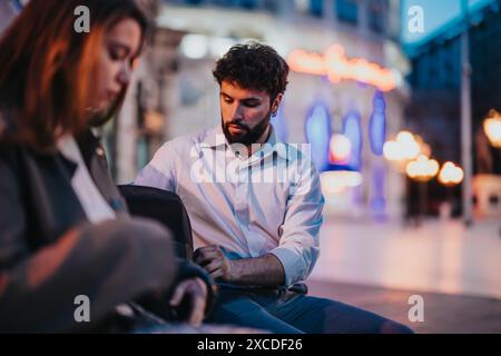 Junges Paar, das nachts auf einer Stadtbank sitzt, konzentriert und in tiefem Gespräch Stockfoto
