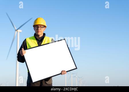 Arbeiter im Helm mit leerem Whiteboard auf einem Feld von Windturbinen. Leer, können Sie Ihren Text hier hinzufügen. Stockfoto
