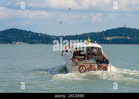 Wassertaxi mit Touristen auf dem Balaton mit dem Hügel Fonyód im Hintergrund. Badacsony, Ungarn, August 31. 2023. Stockfoto