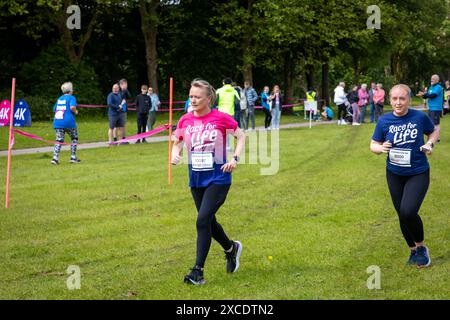 Warrington, Cheshire, Großbritannien. Juni 2024. Das jährlich stattfindende 10K-Rennen um das Leben zur Unterstützung von Cancer Research UK fand im Victoria Park, Warrington, statt. Zwei Frauen in den Race for Life-Trikots gehen auf den Platz. Quelle: John Hopkins/Alamy Live News Stockfoto