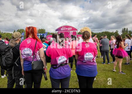 Warrington, Cheshire, Großbritannien. Juni 2024. Das jährlich stattfindende 10K-Rennen um das Leben zur Unterstützung von Cancer Research UK fand im Victoria Park, Warrington, statt. Drei Frauen in Race for Life Shirts hören sich die Anweisungen vor dem Rennen an. Quelle: John Hopkins/Alamy Live News Stockfoto