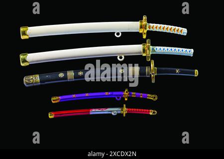 Nahaufnahme einer Sammlung von Miniatur-Spielzeugschwertern in Degen, einschließlich Katana und Wakizashi isoliert auf schwarzem Hintergrund. Stockfoto