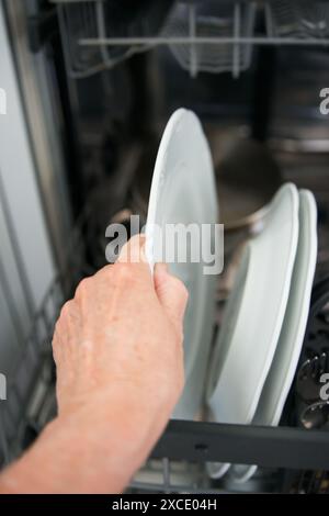 Nicht erkennbare Frau, die Geschirr aus der Geschirrspülmaschine herausnimmt. Kaukasischer Erwachsener Stockfoto
