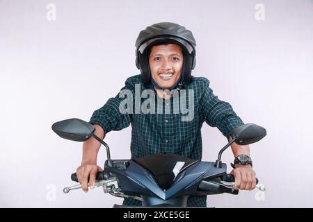 Reifer asiatischer Mann posiert auf einem schnellen Motorrad, spricht während der Fahrt auf dem Handy, trägt Helm, blickt mit fröhlichem Ausdruck nach vorne, isoliert auf Witz Stockfoto