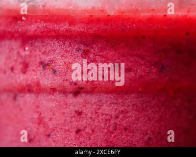 Eine Makroaufnahme eines Smoothies mit rosafarbenen roten Beeren in einer Tasse, die seine detaillierte Textur und leuchtende Farbe zeigt. Stockfoto