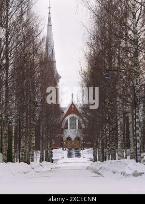 Von Bäumen gesäumte Straße mit Schnee, die zur christlichen Kirche führt Stockfoto