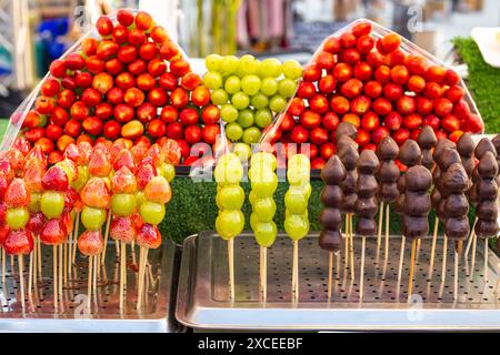 Reife rote Erdbeeren und Trauben auf Spießen in Zuckersirup und Schokoladenglasur. Erdbeeren im Glas. Street Food, leckeres Dessert. Stockfoto