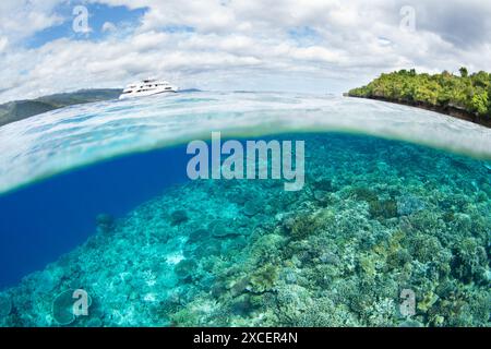 Ein kleines Tauchboot schwimmt direkt vor der Küste in der Nähe eines wunderschönen Korallenriffs in Alor, Indonesien. Diese landschaftlich reizvolle Region bietet eine außergewöhnliche biologische Vielfalt. Stockfoto