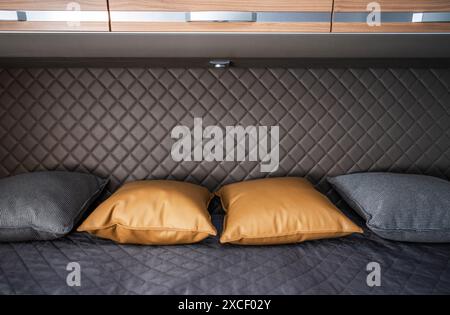 Eine Nahaufnahme eines Bettes in einem modernen Wohnmobil. Das Bett ist mit dunkelgrauer Bettwäsche und drei Kissen ausgestattet. Zwei Kissen sind aus einem Braun Stockfoto