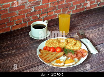 Herzhaftes und nahrhaftes Frühstück, Rührei, knuspriger Speck, Croutons, Kartoffelrösti, schwarzer Kaffee und Orangensaft. Nahaufnahme. Stockfoto