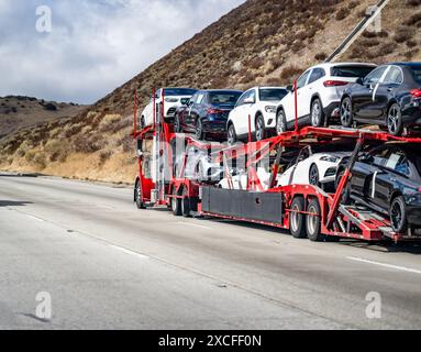 Industrieträger-getriebenes Tagesfahrerhaus großes Fahrzeug, weißer Sattelzugwagen, Sattelzugmaschine für den Transport von Pkw und Crossovers auf hydraulischem zweistufigem rotem Sattelzug Stockfoto