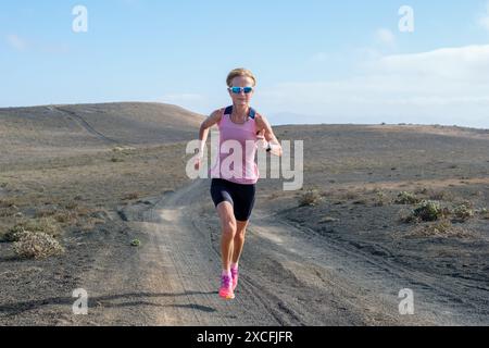 Frau in sportlicher Kleidung, die auf einem verlassenen Weg auf einem offenen Hügel läuft. Stockfoto