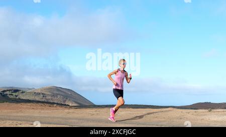 Eine Frau in einem pinkfarbenen Oberteil und schwarzen Shorts rennt durch eine einsame Landschaft und hält auf felsigen Pfaden ein ruhiges Tempo. Ihr lebhaftes Outfit steht im Kontrast Stockfoto