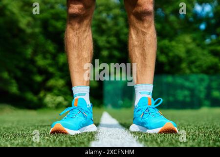 Athlet trägt leuchtend blaue Laufschuhe auf grünem Gras auf dem Sportplatz während des Trainings. Sportlerbeine in Sportschuhen auf der Rennstrecke. Fitness und er Stockfoto