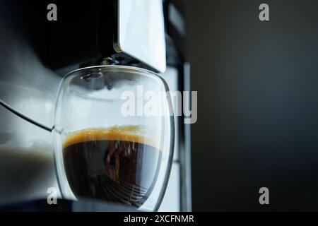 Frischer Espresso in klarem Glas am Morgen. Kaffeemaschine auf dunklem Hintergrund, Nahaufnahme. Moderne Kaffeemaschine mit frisch gebrühtem Kaffee in Glasbecher. Ki Stockfoto