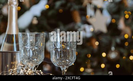 Eine Flasche Champagner und zwei Weingläser stehen auf einem Tisch neben einem Weihnachtsbaum. Die Szene ist festlich und feierlich, mit Champagner. Stockfoto