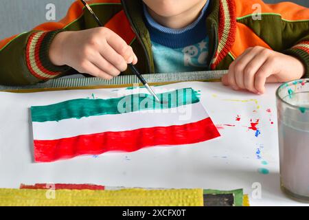 Der Junge zieht die Flagge Tadschikistans mit Aquarellen auf ein Pergamentblatt. Stockfoto