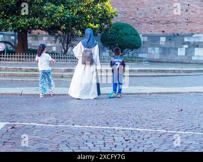 Cremona, Italien - 10. Juni 2024 die muslimische Familie genießt einen Tag mit Motorrollern auf einer kopfsteingepflasterten Straße Stockfoto