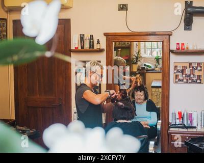 Cremona, Italien - 10. Juni 2024 Friseur, der die Haare eines Kunden in einem Friseursalon stylt. Der eine föhnt, der andere verwendet ein Lockenstab Stockfoto