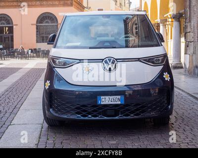 Cremona, Italien - 10. Juni 2024 ein moderner elektrischer Volkswagen-Van mit Gänseblümchendekor steht auf einem Kopfsteinpflasterplatz in einer italienischen Stadt Stockfoto