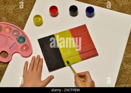 Die belgische Flagge wird von einem Jungen auf einem Blatt Papier mit Aquarellen und einem Pinsel gezeichnet. Stockfoto