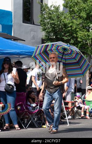 Während der Pride Parade 2024 in Albuquerque, New Mexico, USA, geht ein großer, markanter Mann die Route 66 hinunter und hält einen großen, blau gestreiften Regenschirm. Stockfoto