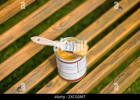 Pinsel und Dose Farbe auf einer Holzbank im Freien öffnen. Die Farbe ist goldgelb und die Bank ist aus natürlichem Holz. Stockfoto