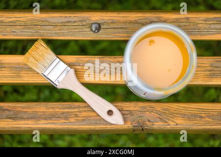 Pinsel und Dose Farbe auf einer Holzbank im Freien öffnen. Die Farbe ist goldgelb und die Bank ist aus natürlichem Holz. Stockfoto