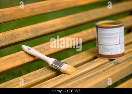 Pinsel und Dose Farbe auf einer Holzbank im Freien öffnen. Die Farbe ist goldgelb und die Bank ist aus natürlichem Holz. Stockfoto