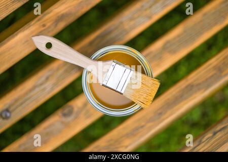 Pinsel und Dose Farbe auf einer Holzbank im Freien öffnen. Die Farbe ist goldgelb und die Bank ist aus natürlichem Holz. Stockfoto