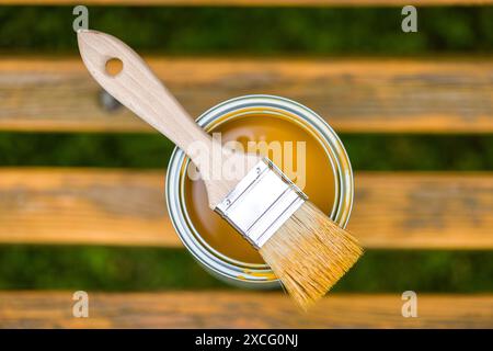 Pinsel und Dose Farbe auf einer Holzbank im Freien öffnen. Die Farbe ist goldgelb und die Bank ist aus natürlichem Holz. Stockfoto