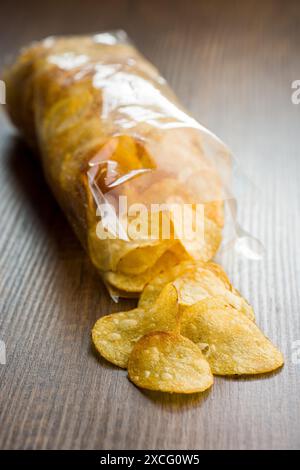 Knusprige Kartoffelchips aus einer Plastiktüte auf einem Holztisch verschüttet Stockfoto