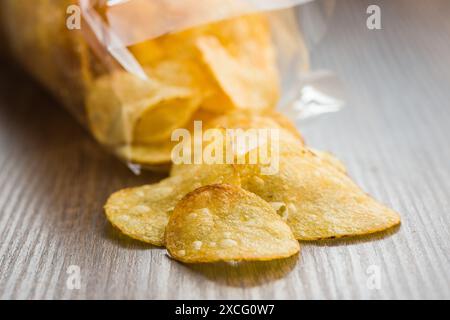 Knusprige Kartoffelchips aus einer Plastiktüte auf einem Holztisch verschüttet Stockfoto